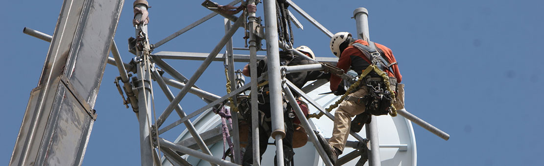 Men connected to safety cables doing some antenna tower checks