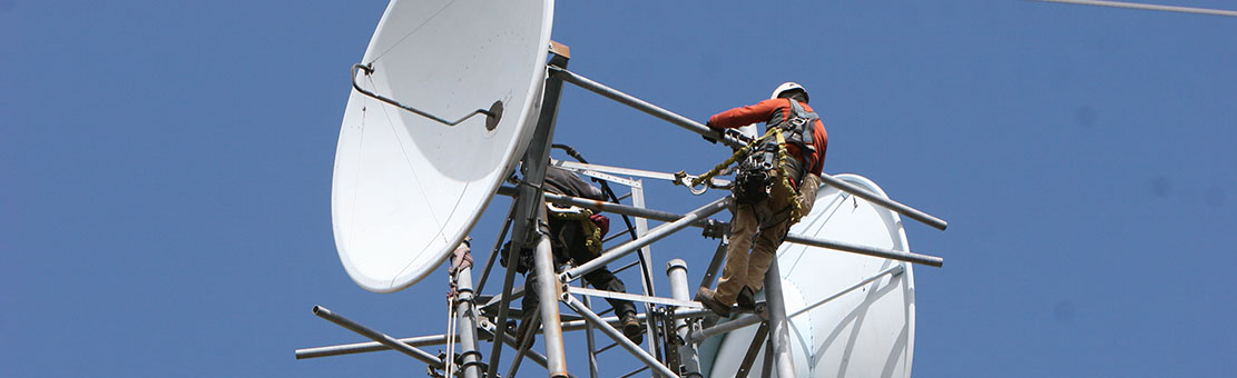 Men connected to safety cables doing some antenna tower checks